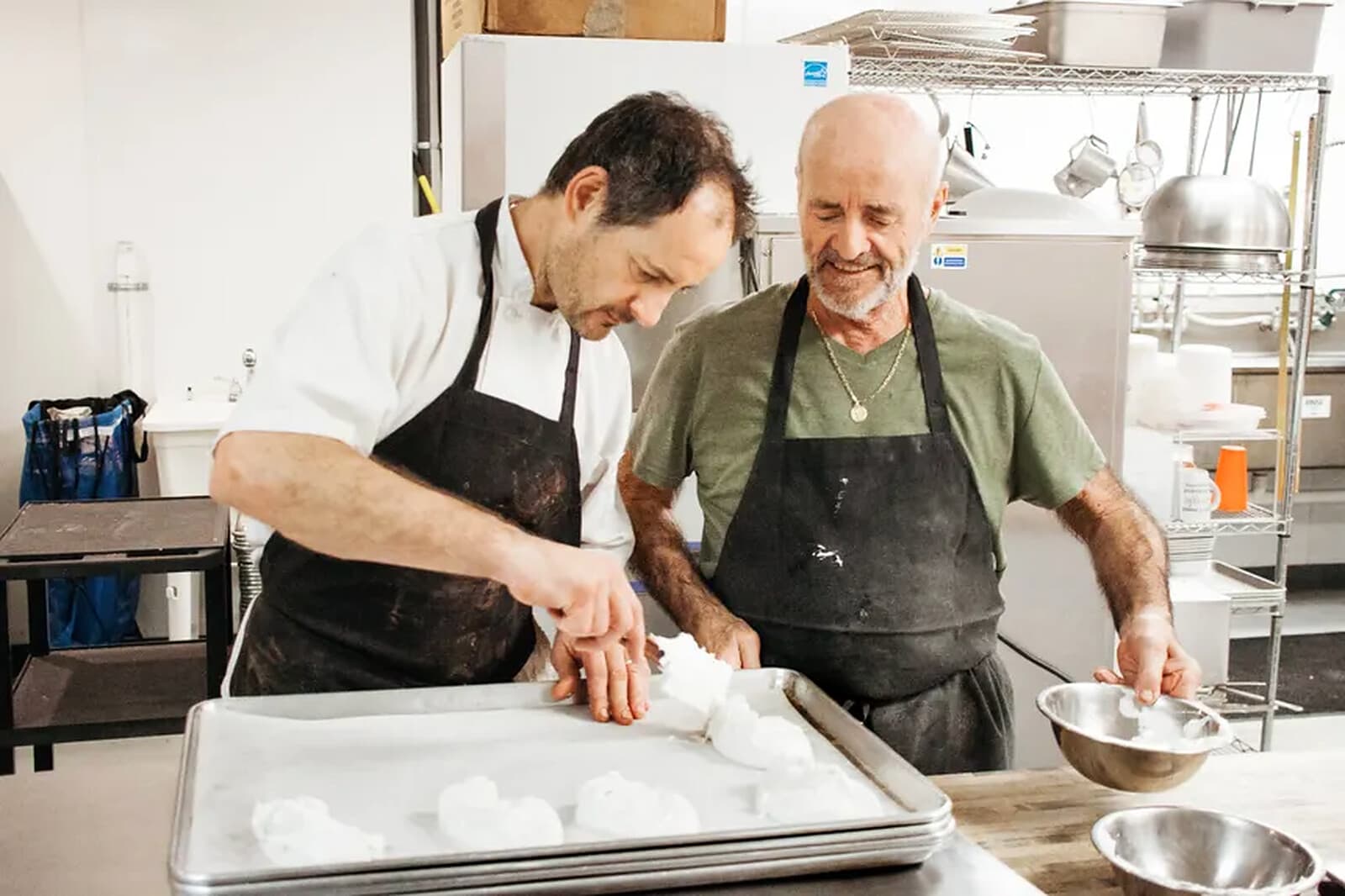 Chef Christophe showing a student how to shape macaron shells onto a baking tray in the shop kitchen